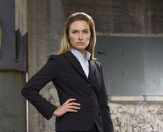 a woman in a business suit standing with her hands on her hips and looking at the camera