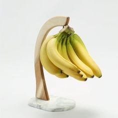 a bunch of bananas hanging from a wooden stand on a marble base with white background