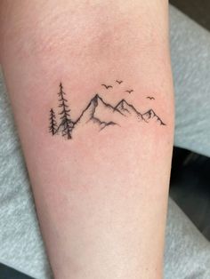 a small tattoo on the leg of a woman with mountains and trees in the background