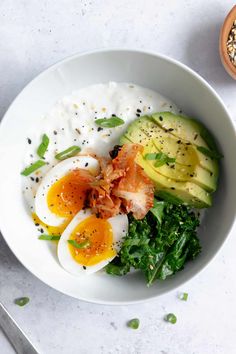 a bowl filled with eggs, avocado and other food on top of a table