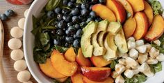 a white bowl filled with fruit and vegetables on top of a wooden table next to an orange slice