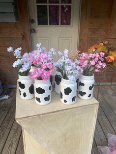 four painted jars with flowers in them sitting on a table next to a front door