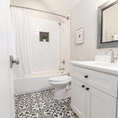 a white bathroom with black and white tile flooring on the shower, toilet and bathtub