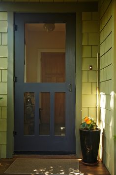 a blue front door with two potted plants on the side and a yellow brick wall behind it