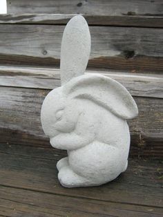 a white rabbit statue sitting on top of a wooden floor next to a fence and wood planks