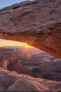 the sun is setting through an opening in a rock formation, overlooking canyons and mountains