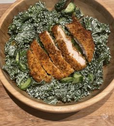 a wooden bowl filled with greens and sliced chicken on top of it's side