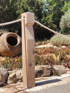 a wooden post next to a stone and roped in area with plants on the other side