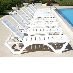 a row of white lawn chairs next to a swimming pool