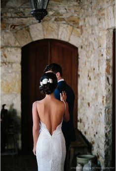 a bride and groom standing in front of a stone building with a light fixture hanging from the ceiling