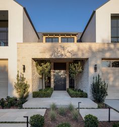 the front entrance to a modern home with two garages and trees on either side