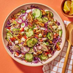 a salad with cucumbers, red cabbage and other vegetables in a bowl next to a wooden spoon