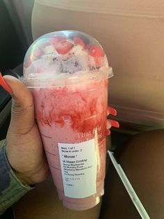 a person holding up a plastic cup with ice and strawberries in it on a plane