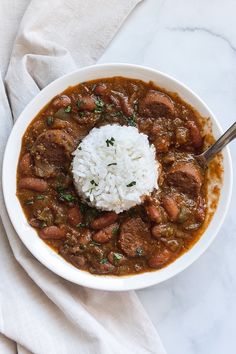 a white bowl filled with meat and rice on top of a table next to a napkin