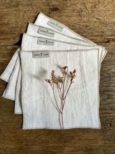 four white linen placemats with dried flowers on them sitting on a wooden table