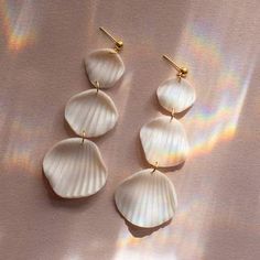 three seashells are hanging from gold earwires on a pink background with iridescent light