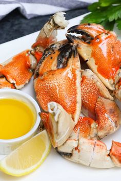 cooked crab legs with lemon and parsley on white platter next to dipping sauce