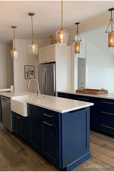 a kitchen with blue cabinets and white counter tops, gold pendant lights over the island