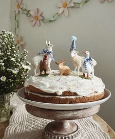 a cake with white frosting and three animals on top, sitting on a table next to flowers