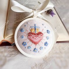 a cross stitch heart ornament on top of an open book