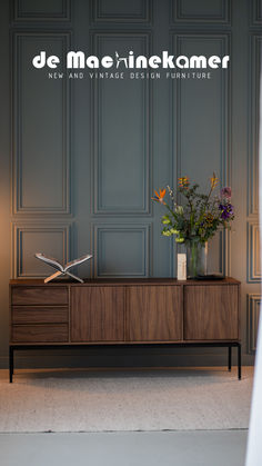 a vase with flowers sitting on top of a wooden cabinet next to a lamp and wall