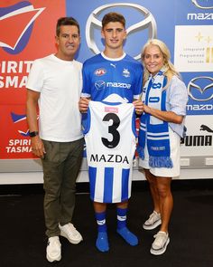 two people standing next to each other with a soccer jersey in front of an advertisement