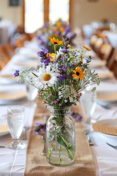 a vase filled with flowers sitting on top of a long table covered in white linen