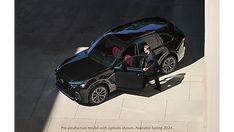 an aerial view of a man in a black suv with the door open, standing next to his car