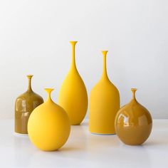 three yellow vases sitting next to each other on a white counter top in front of a white wall