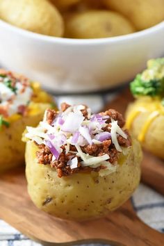 three baked potatoes with meat and cheese on top, next to a bowl of broccoli