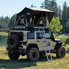 a jeep with a tent on the roof parked in front of a body of water