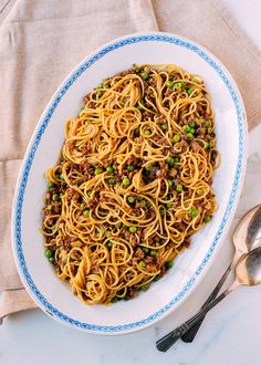 a white bowl filled with noodles and peas on top of a table next to two spoons