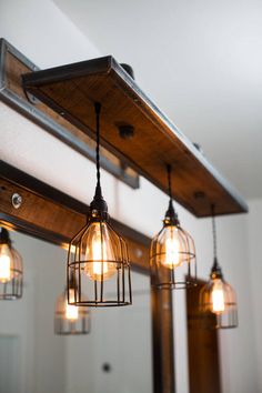 three light fixtures hanging from a wooden beam in a bathroom with mirrors and lights on the wall