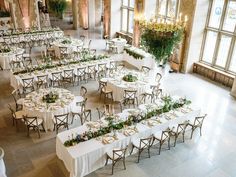 tables with white linens and greenery are set up in the middle of a large hall