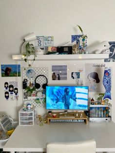 a white desk with a computer monitor on top of it next to some pictures and plants