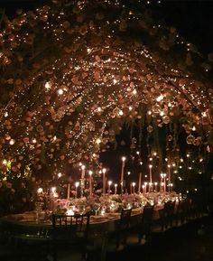 a table with candles and flowers on it under a canopy covered in lights at night