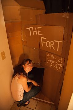 a woman sitting on the floor in front of a cardboard box with writing on it that says, i enjoy making pillow forts i'm 48