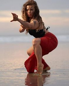 a woman in a black top and red skirt is dancing on the beach