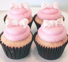 three cupcakes with pink frosting and bows on them sitting on a plate