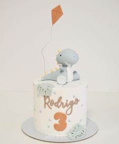 a baby's first birthday cake with a dinosaur on top and a kite in the air