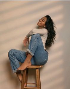 a woman sitting on top of a wooden stool with her legs crossed and eyes closed