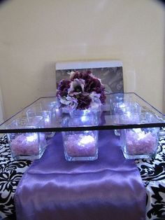 a table topped with vases filled with purple flowers and candles on top of it