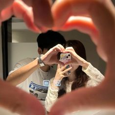 two people taking pictures in front of a mirror with their cell phones and hands holding up the camera