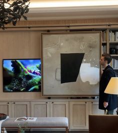 a man standing in front of a flat screen tv next to a living room filled with furniture