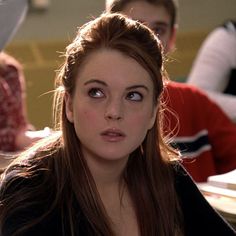 a woman with long hair sitting at a table in front of other people and looking off to the side