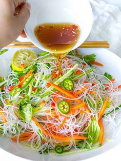 someone is pouring sauce on a salad in a white bowl with noodles and veggies