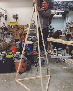 a man standing on top of a wooden ladder in a garage next to other tools