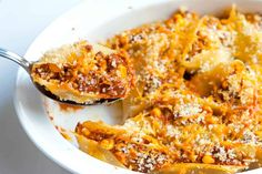 a white bowl filled with pasta covered in sauce and cheese, next to a spoon