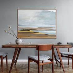 a dining room table with two chairs and a painting hanging on the wall above it