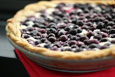 a pie with blueberries and cream on top is sitting on a red napkin next to a window